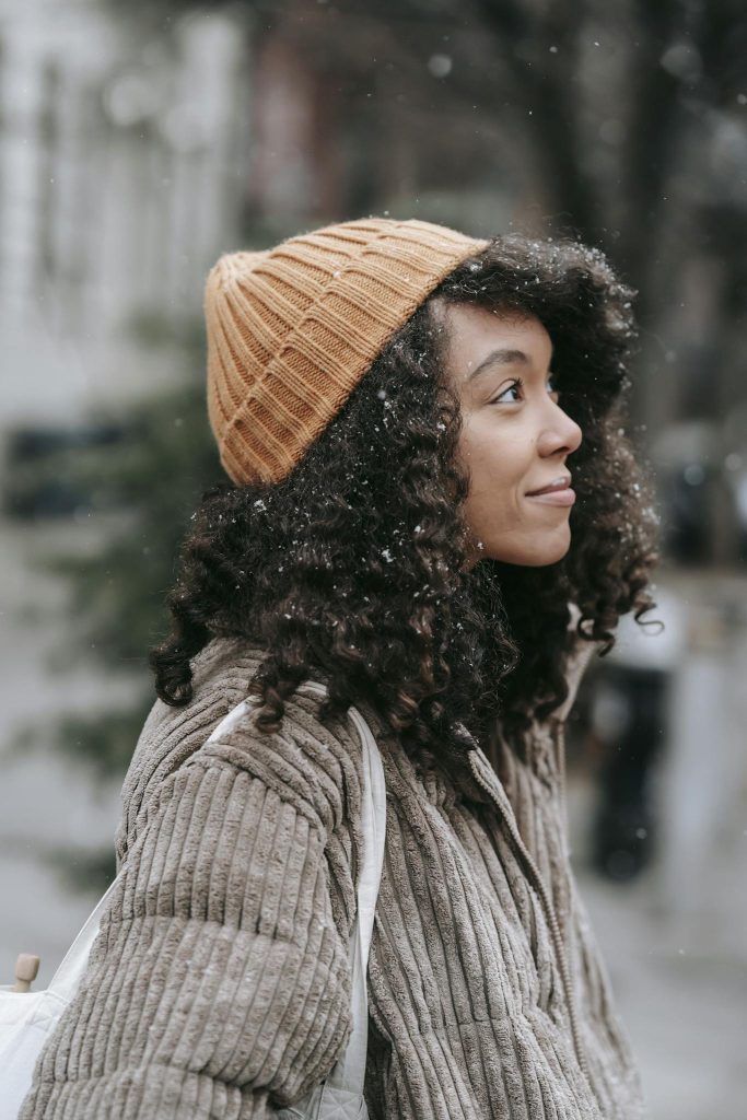 Contemplative ethnic woman with curly hair in snowfall